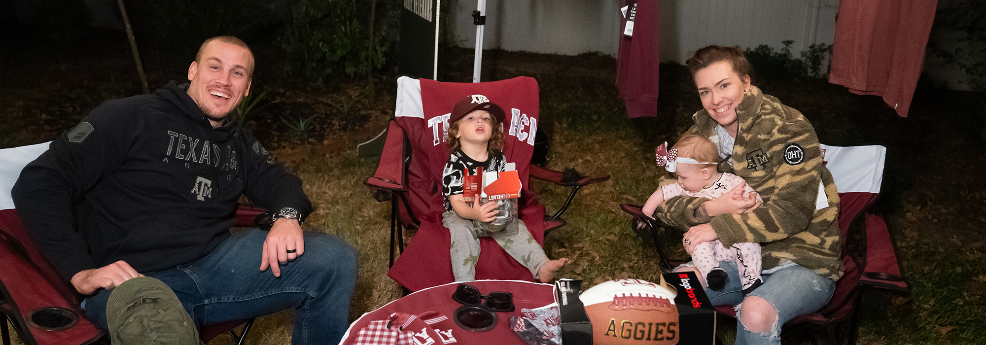 Man and wife with their two children sit in their backyard after the TAMU team surprised them with an Operation Hat Trick prize package. 