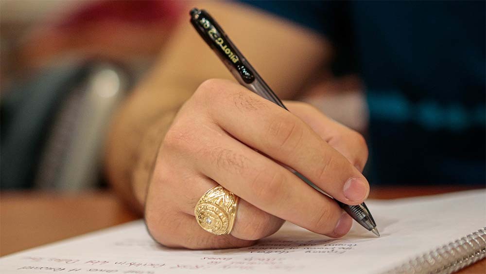 Person wearing an aggie ring writes on a piece of paper