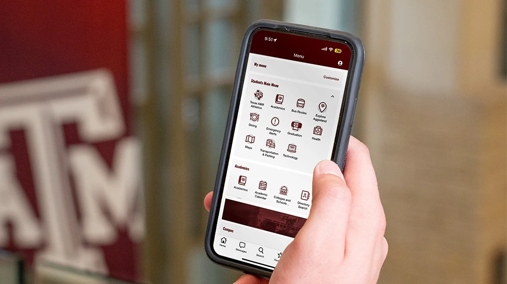 A hand holding a phone with the Texas A&M mobile app on screen