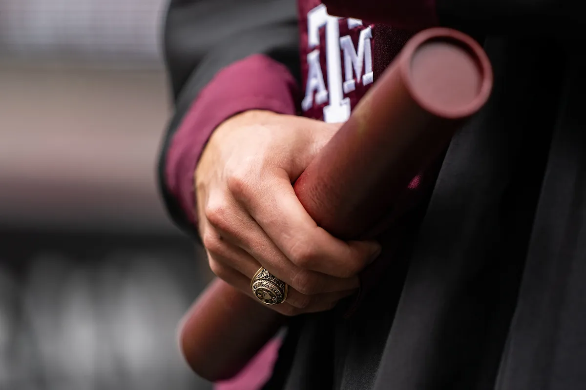 Closeup of an Aggie gripping his diploma in the same hand that wears his Aggie Ring