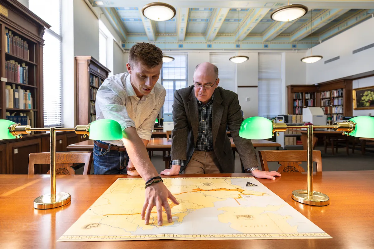 A student points out a place on a map to his professor in a library